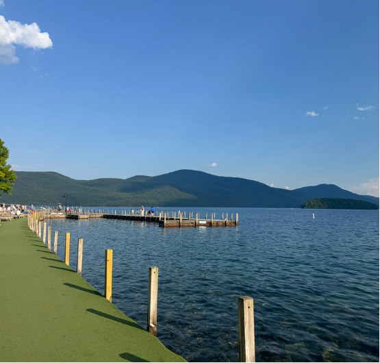 A long wooden dock reaching into Lake George, with mountains beyond